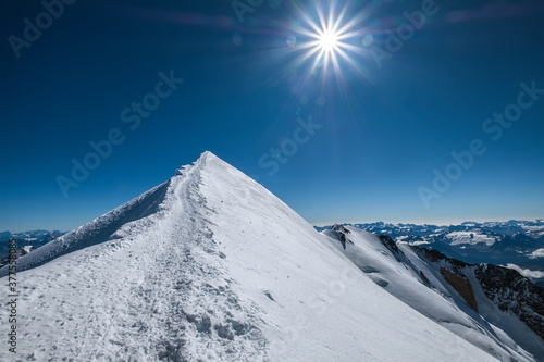 Mont Blanc (Monte Bianco) snowy 4808m summit wide angle view with surrounded French Alps landscape with deep blue sky and bright midday sun. Popular nature landmarks concept image.