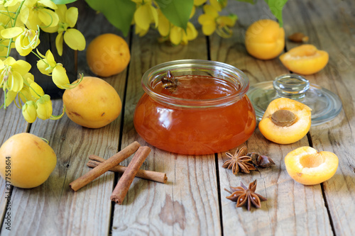 Apricot jam, in a glass jar with anise and cinnamon on a wooden table with apricots and flowers.