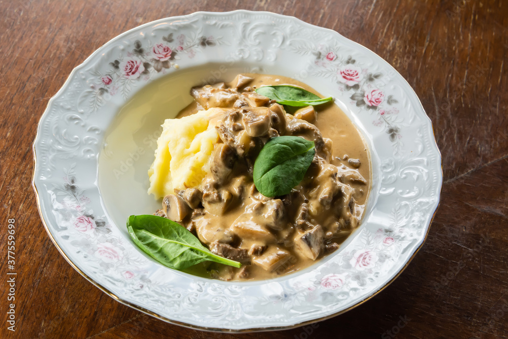 Plate of beef stroganoff with mashed potatoes and greens