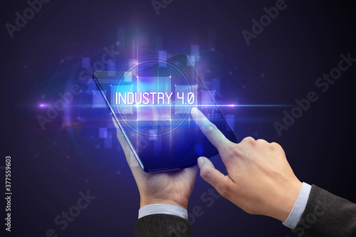 Businessman holding a foldable smartphone with INDUSTRY 4.0 inscription, new technology concept