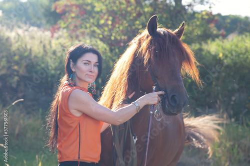pretty girl with beautiful chestnut stallion with long mane against stone green bushes wall