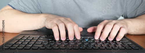 mężczyzna piszący na klawiaturze, laptopie, praca zdalna w domu, biurowa, ręce na klawiaturze, widok naprzeciw monitora, ekranu