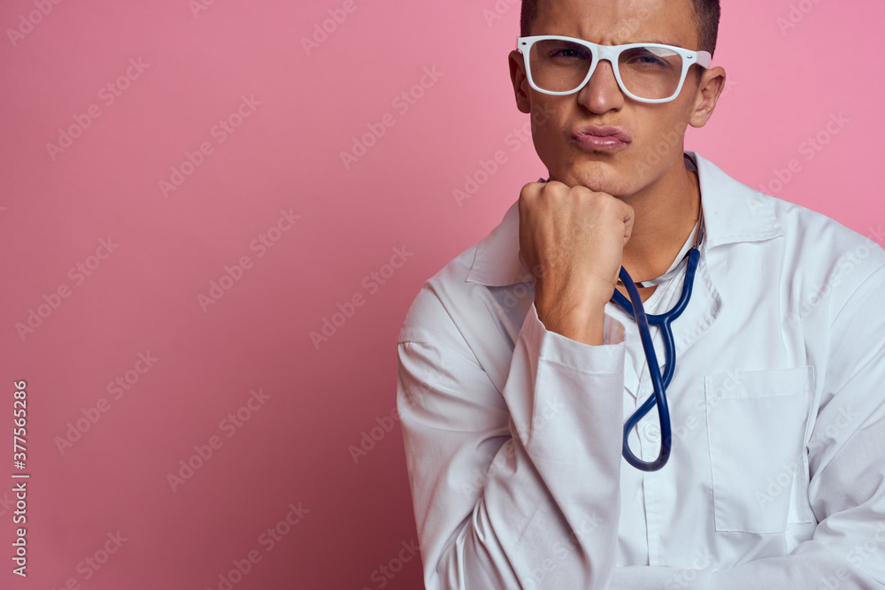 male doctor in a medical gown with a stethoscope around his neck on a pink background and glasses on his face male doctor in a medical gown with a stethoscope around his neck on a pink background and glasses on his face