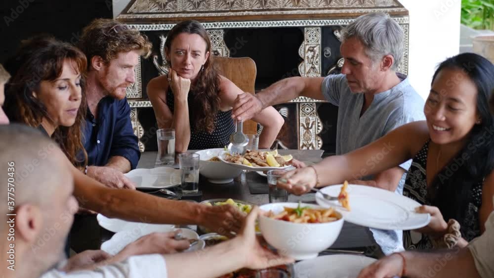 Diverse group of multiethnic friends enjoying meal sharing and passing food to each other in outdoor cafe or home. Leisure, food and drinks, people and holidays concept Diverse group of multiethnic friends enjoying meal sharing and passing food to each other in outdoor cafe or home. Leisure, food and drinks, people and holidays concept