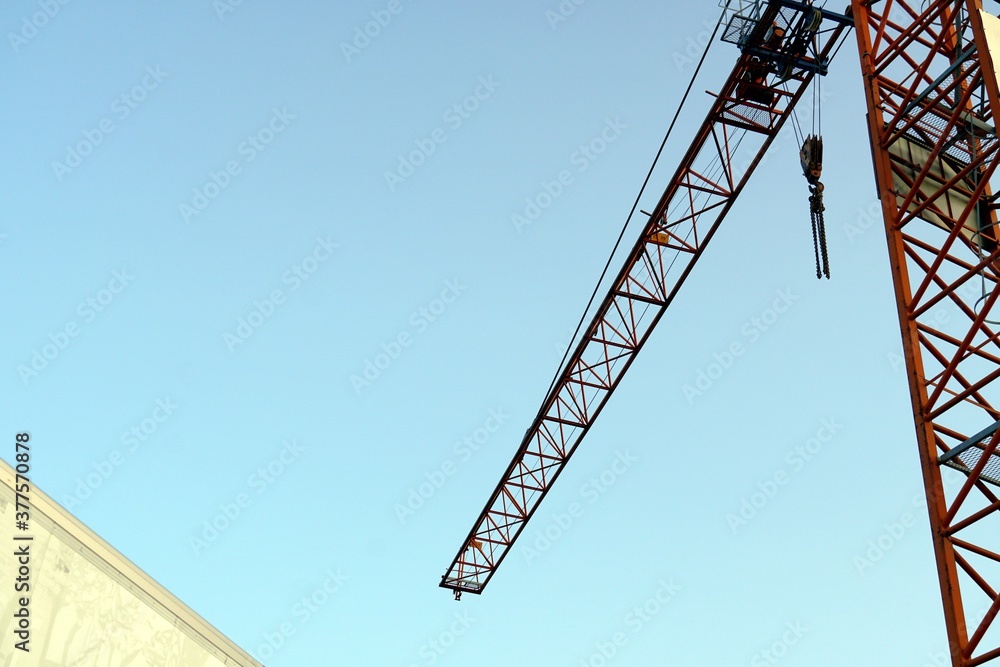 An industrial crane with a stretched arm and a hook and chain hanging down from it. The photo with a lot fo copy space.