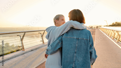 Lesbian couple standing on the bridge, embracing each other while admiring the sunrise together. Homosexuality, LGBT and love concept