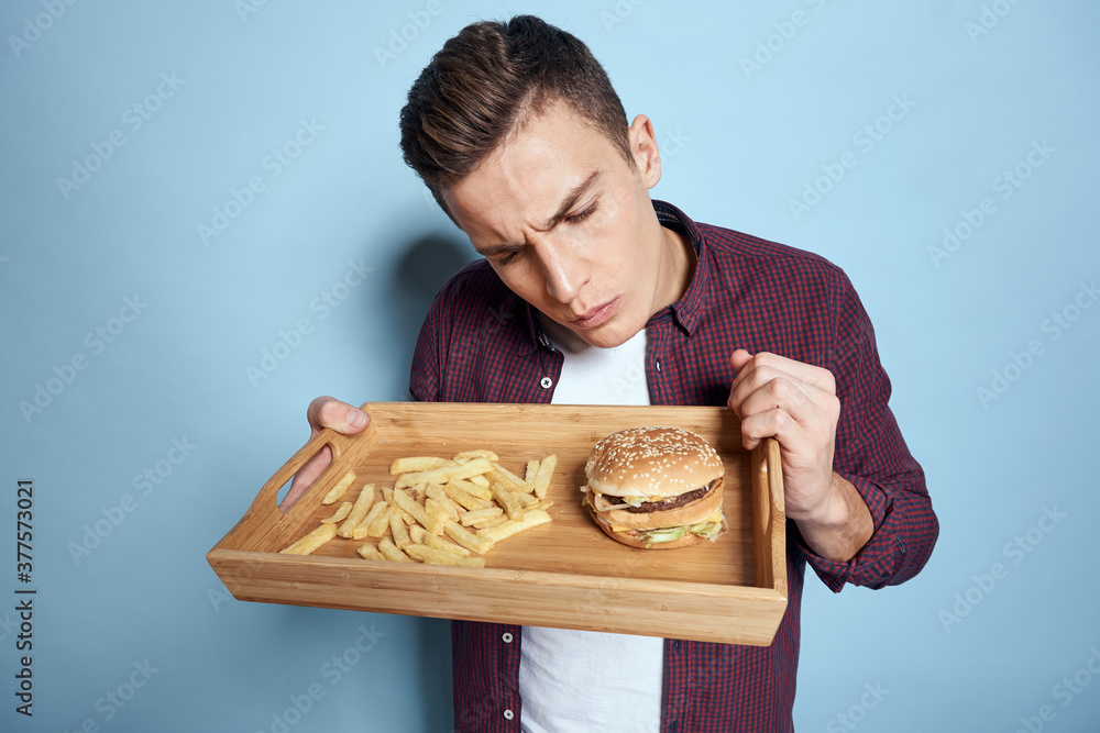 Man with wooden pallet fast food french fries hamburger hunger diet food blue background Man with wooden pallet fast food french fries hamburger hunger diet food blue background