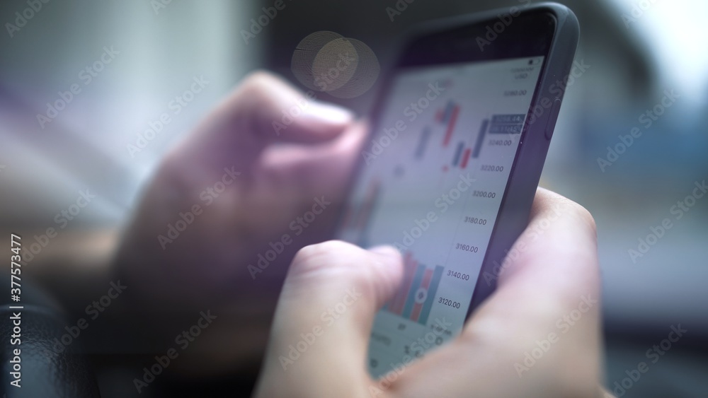 Hands with a mobile phone, checking stock market data. Smartphone with stock market graph on a touch screen device close up, blurred with bokeh effect Hands with a mobile phone, checking stock market data. Smartphone with stock market graph on a touch screen device close up, blurred with bokeh effect