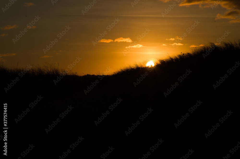 Sundown over silhouette of sand dunes along the seashore