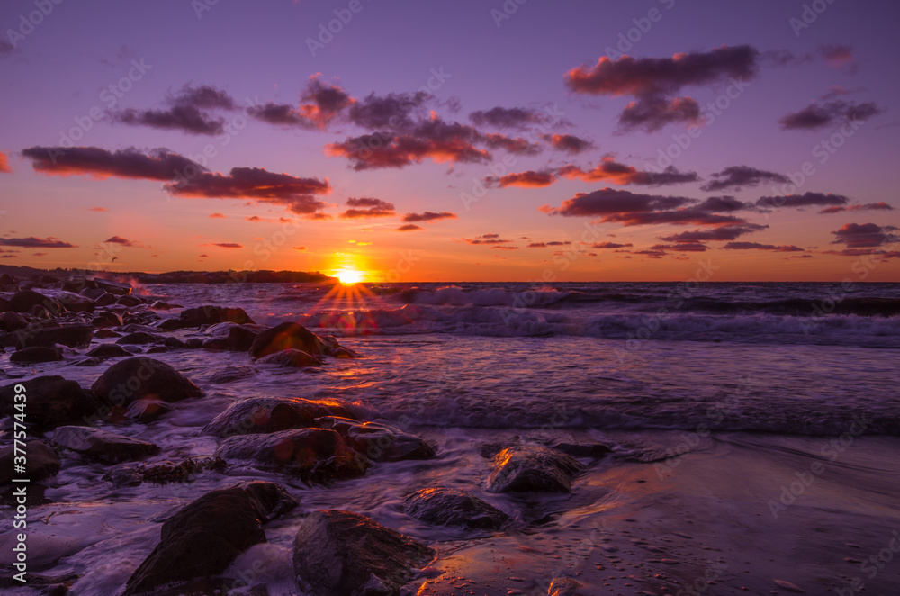 Purple sunset over rocky harbor along a beach with colorful clouds in the sky