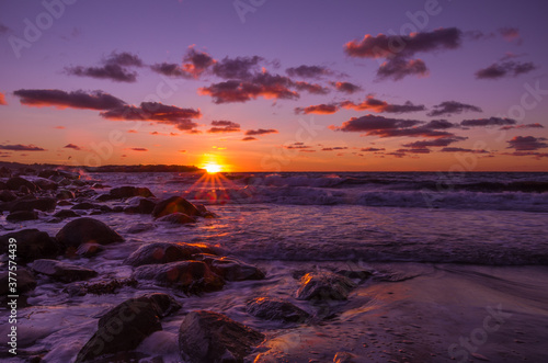Purple sunset over rocky harbor along a beach with colorful clouds in the sky