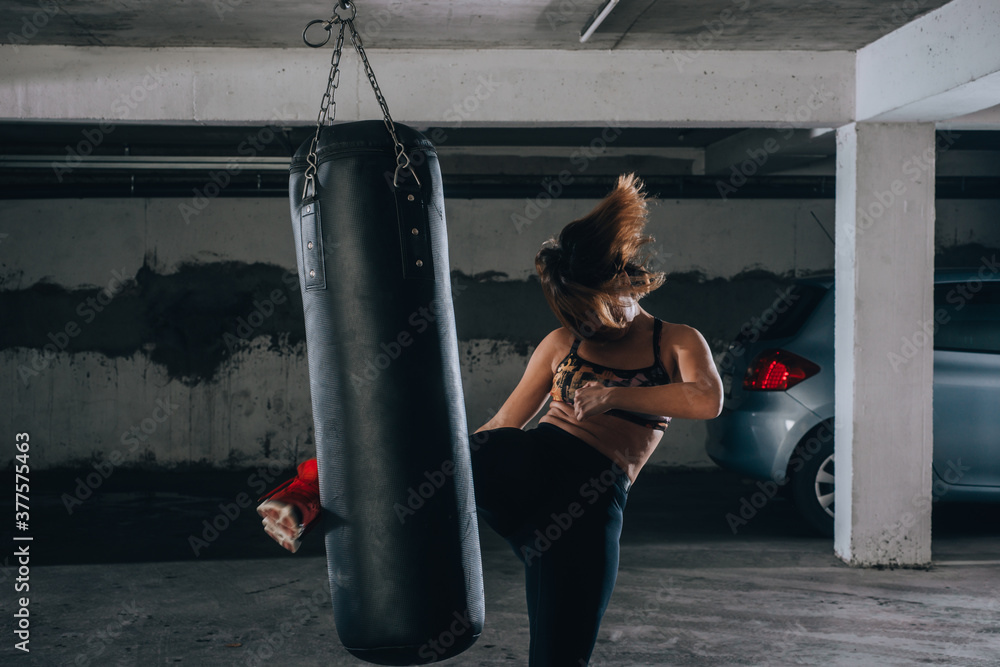 Young sportswoman doing high kick during boxing exercise in a garage.