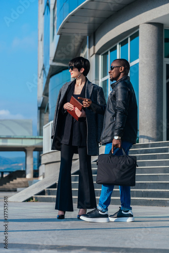 Full-length portrait of african businessman and caucasian businesswoman waiting for their colleague in front of their office building photo