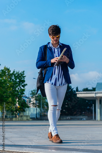 Full-length picture of a handsome young businessman standing outdoors with documents, mobile phone and briefcase. photo