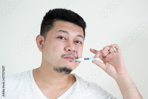 people, healthcare and fever concept - unhealthy asian man measuring oral temperature by thermometer over white background