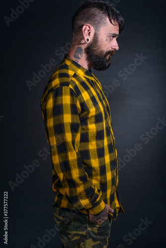 Profile portrait picture of a bearded man with tattoos on his face and neck in yellow black shirt