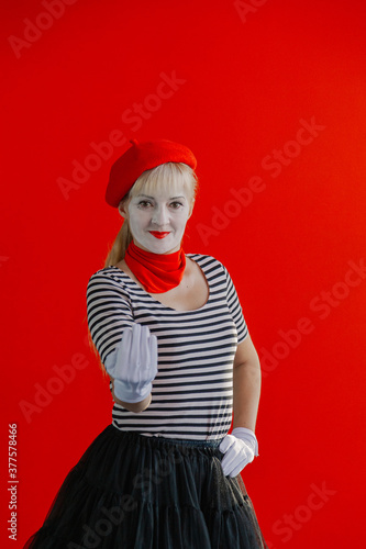 Woman mime near a red wall in a red beret shows a sign with her hand.