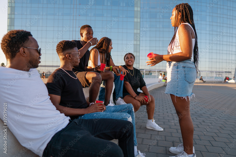 Group of young modern african black friends happily sitting together on the bench of the stairs in bright sunlight enjoying summer vacation Group of young modern african black friends happily sitting together on the bench of the stairs in bright sunlight enjoying summer vacation