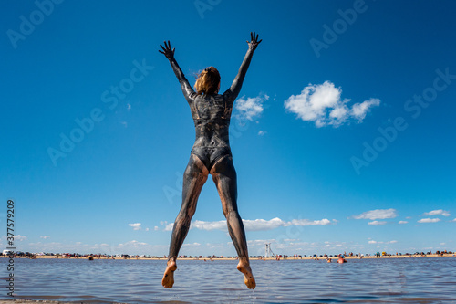 A girl covered with medical mud jumps against the background of the sea photo