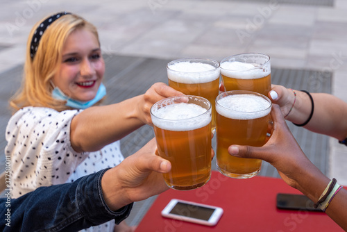 group of multi-ethnic friends toast raising glasses of beer, focus on the four raised beers and the hands of millenials toasting, blonde girl in the background