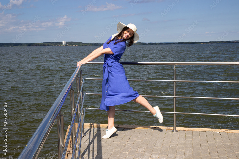 Young woman in hat on pier in stylish elegant dress poses enjoying amazing view.