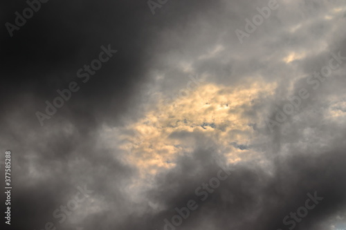 patch of sky with clouds illuminated by twilight light, surrounded by thin gray clouds.