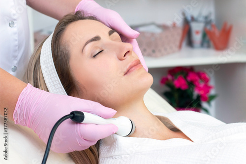 Hardware cosmetology. Close up picture of lovely young woman with closed eyes receiving rf lifting procedure in beauty salon.