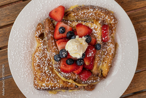 French toast topped with blue. berries, sliced strawberries, powdered sugar and butter makes a delicious breakfast meal. photo