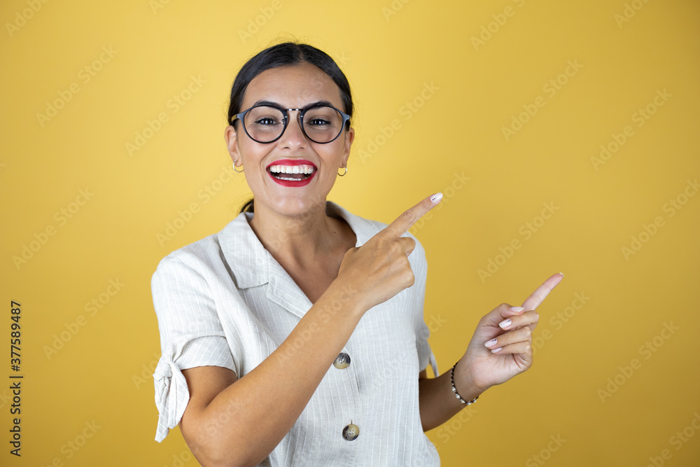 Beautiful woman over yellow background surprised and pointing with hand and finger to the side Beautiful woman over yellow background surprised and pointing with hand and finger to the side