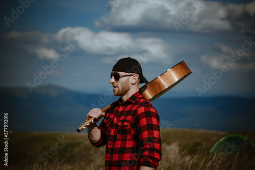 Traveling, hopster man. Hiker guy with guitar near mountain landscape. photo