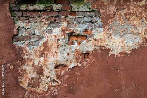 Old brown wall. Background walls with partially fallen off plaster. Background from the facade of an old house. Vintage construction background. A crumbling wall with bricks. Moss on old masonry.