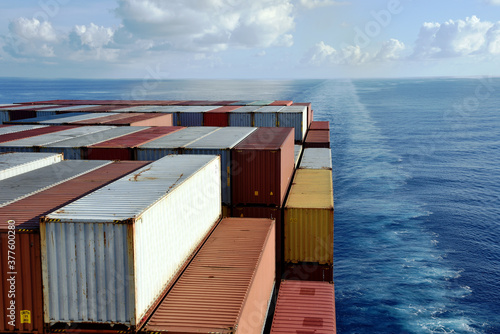 Fully loaded container ship sailing through a blue, calm ocean. View on the stack of the containers loaded on the aft of the cargo ship.