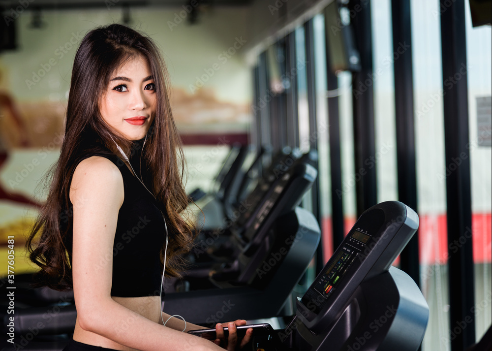 Fototapeta premium Young woman using technology mobile smartphone play music exercise workout on treadmill at fitness gym