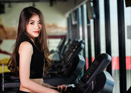 Young woman using technology mobile smartphone play music exercise workout on treadmill at fitness gym