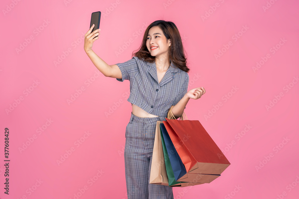 Asian woman online shopping bag using smartphone mobile technology device purchasing products payment happy joyful smiling beautiful attractive one person, model studio pink isolated background Asian woman online shopping bag using smartphone mobile technology device purchasing products payment happy joyful smiling beautiful attractive one person, model studio pink isolated background