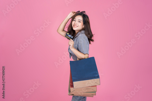 Asian woman online shopping bag promotion sales using credit card purchasing products online transaction payment happy smiling beautiful attractive one person, model studio pink isolated background