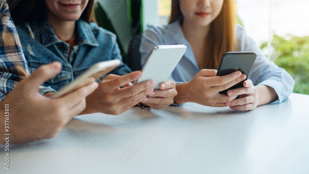 Group of young people using and looking at mobile phone while sitting together Group of young people using and looking at mobile phone while sitting together