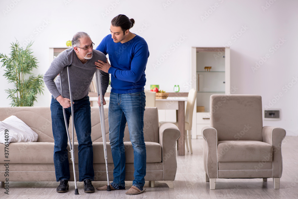 Young man looking after his leg injured father Young man looking after his leg injured father