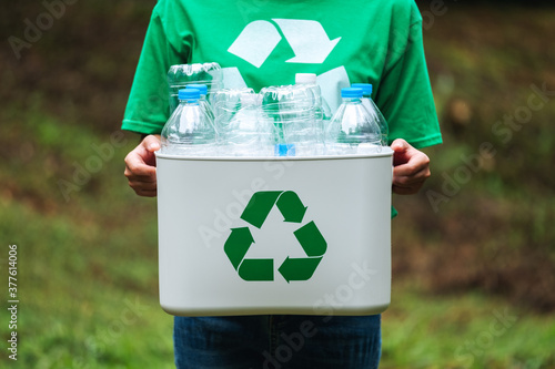 A woman holding a recycle bin with plastic bottles in the outdoors