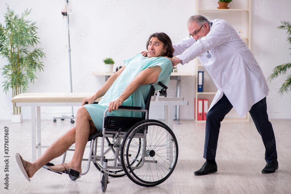 Young male patient in wheel-chair and experienced doctor traumatologist Young male patient in wheel-chair and experienced doctor traumatologist