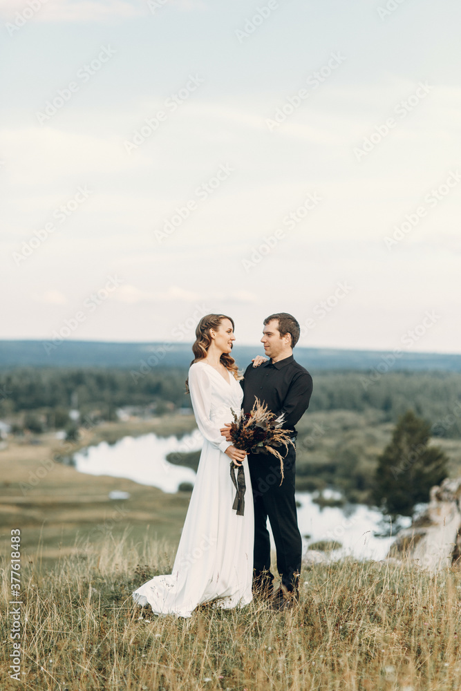 A beautiful fairy-tale happy bride with a bouquet and a wreath and a stylish groom on the background of rocks in the mountains. Boho wedding in nature. A beautiful fairy-tale happy bride with a bouquet and a wreath and a stylish groom on the background of rocks in the mountains. Boho wedding in nature.