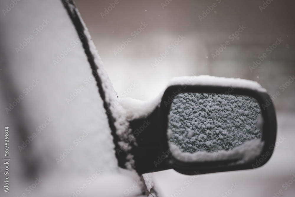 Early winter. Unexpected snow covered cars and roads. Door mirror and glass of a car in the snow. Road safety. Toning