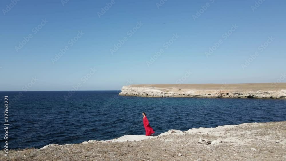 brunette woman in a red long dress walk on the edge of a cliff by the sea in summer in the Crimea brunette woman in a red long dress walk on the edge of a cliff by the sea in summer in the Crimea