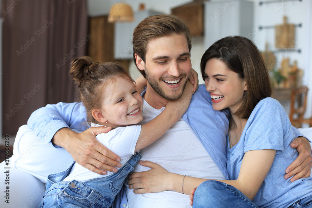 Positive friendly young parents with smiling little daughter sitting on sofa together while relaxing at home on weekend. Positive friendly young parents with smiling little daughter sitting on sofa together while relaxing at home on weekend.
