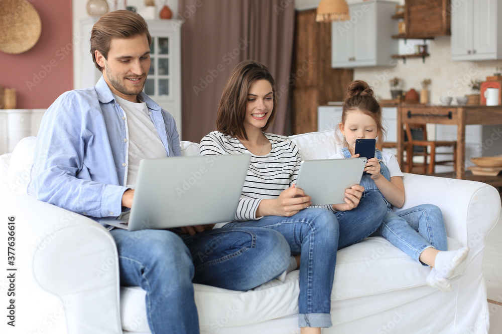 Father, mother and daughter using electronic devices sitting on sofa at living room. Father, mother and daughter using electronic devices sitting on sofa at living room.