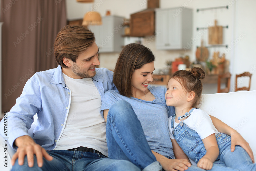 Positive friendly young parents with smiling little daughter sitting on sofa together while relaxing at home on weekend. Positive friendly young parents with smiling little daughter sitting on sofa together while relaxing at home on weekend.