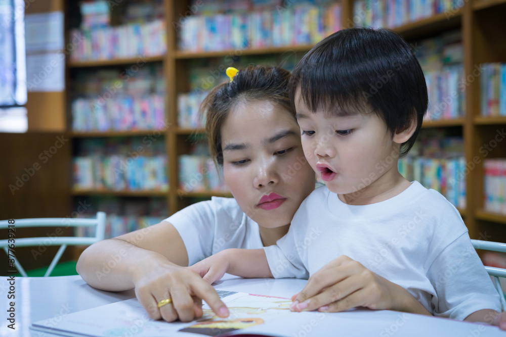 Asian young mother with little boy reading book together in library. Happy family. Parent educating children. Pre-school learning concept. Asian young mother with little boy reading book together in library. Happy family. Parent educating children. Pre-school learning concept.