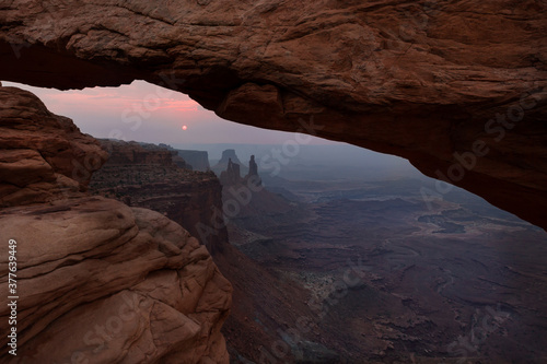 Sunrise viewed through Mesa Arch in the Canyonland National Park in Utah. Unique light effect created by the haze from the further fires in Colorado