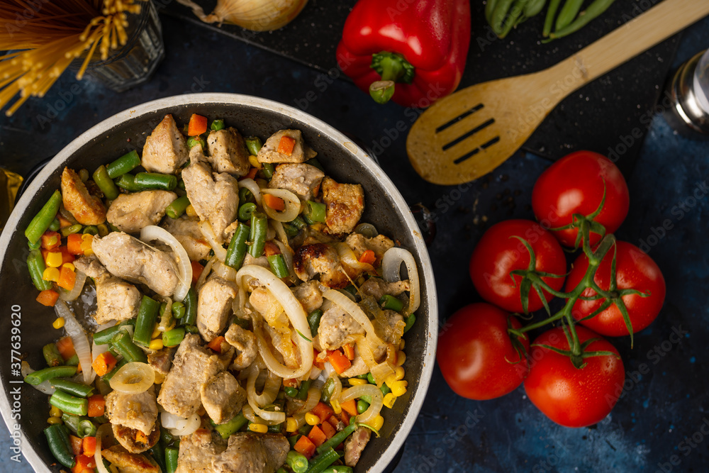 Grilled meat with different vegetables in frying pan isolated on dark background. Red pepper. cherry, cutlery, green peas and spaghetti for decoration photo. Cooking tasty meat. Restaurant food.