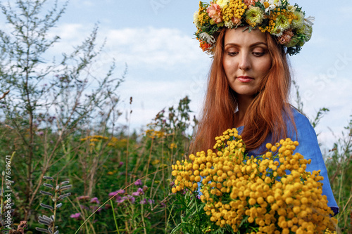 Slavic beauty with a floral wreath on her head and a bouquet of wildflowers. Ancient pagan origin celebration concept. Summer solstice day. Mid summer. Ancient rituals. photo